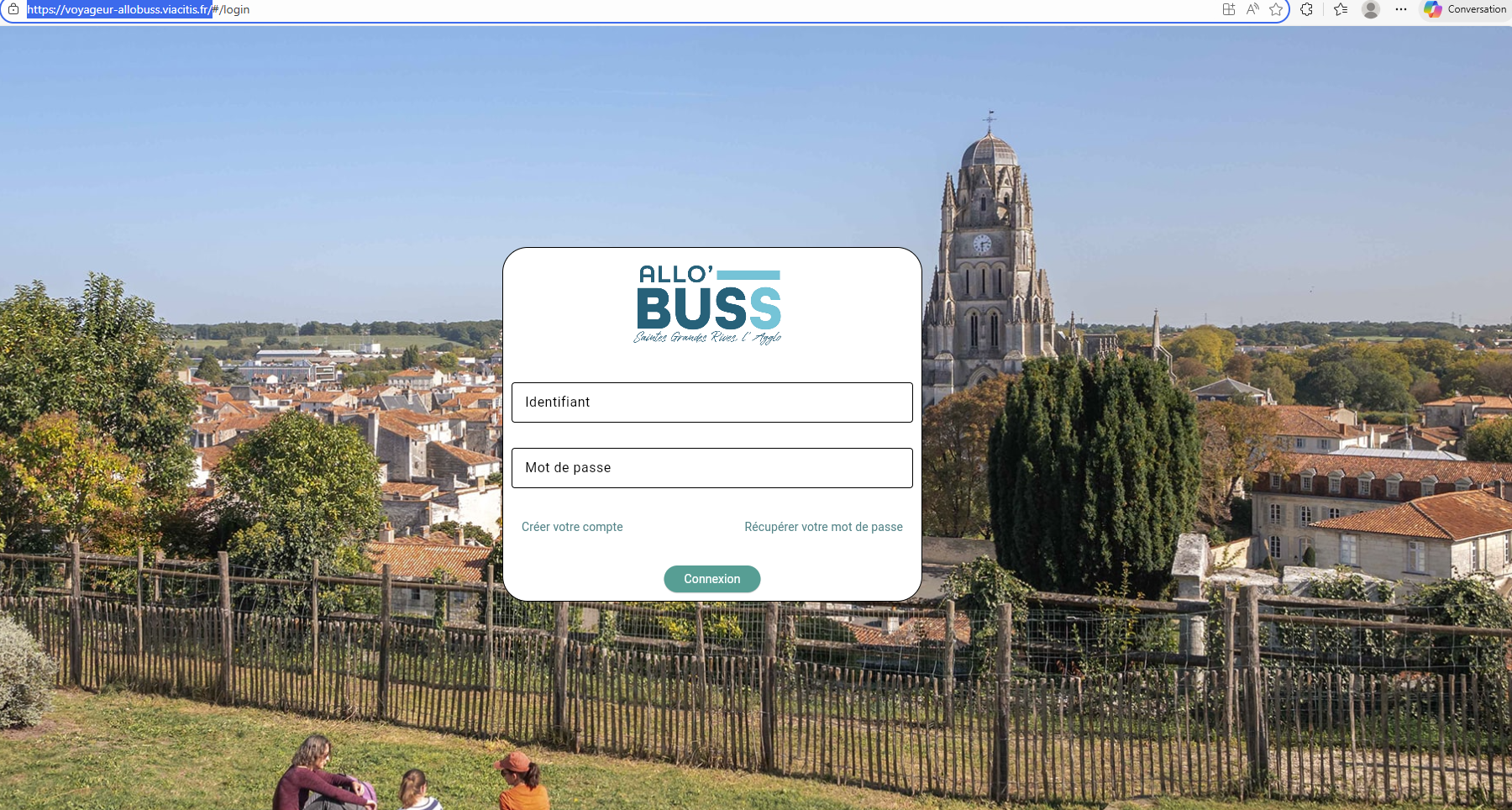 age de connexion du service « Allo’ Buss ». Au centre, un formulaire avec deux champs intitulés « Identifiant » et « Mot de passe », un bouton « Connexion », ainsi que des liens pour créer un compte ou récupérer son mot de passe. En arrière-plan, une vue panoramique d’une ville avec des toits en tuiles, des arbres, une clôture en bois au premier plan, et une grande église avec un clocher dominant le paysage.
